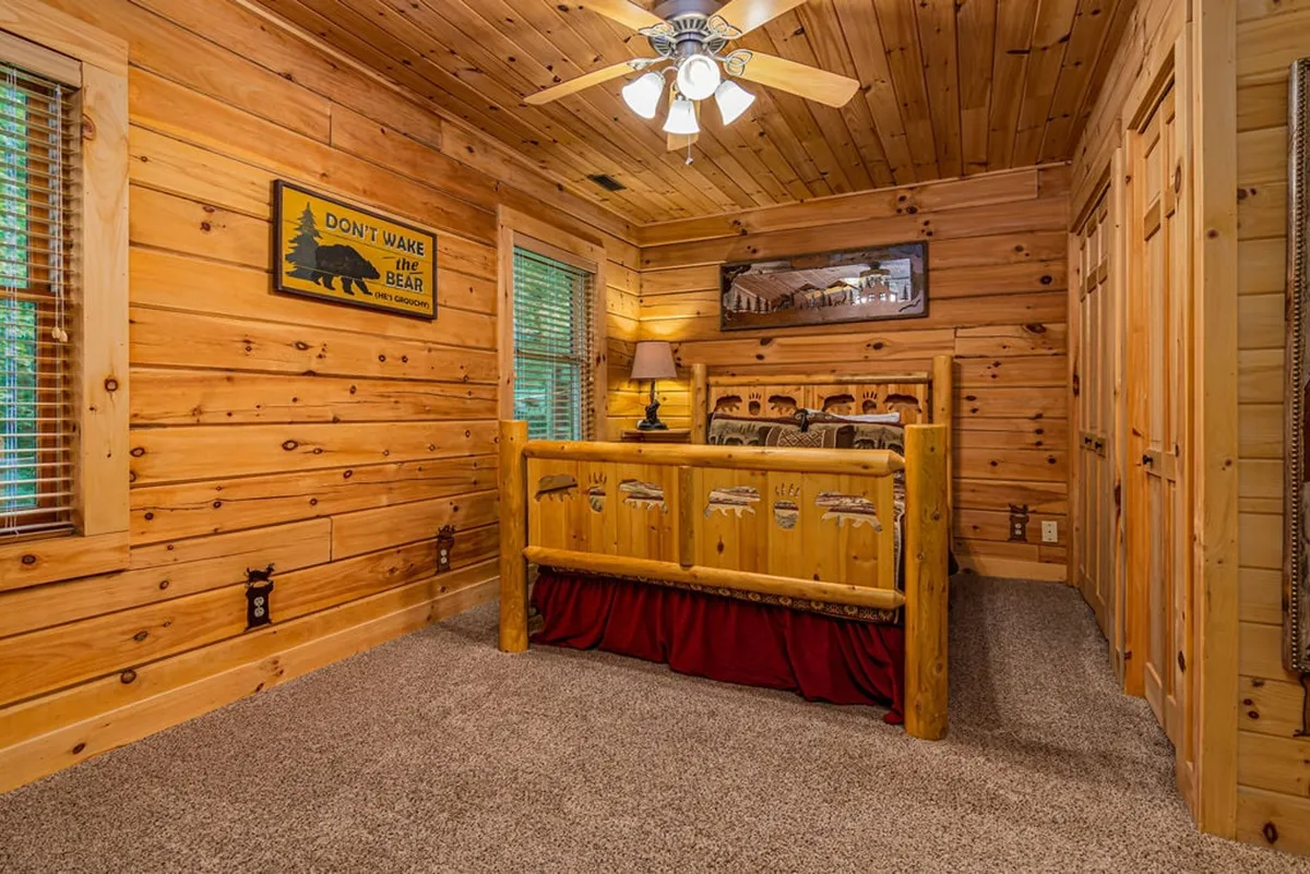 A bear-themed queen bedroom with a comfortable wooden bed frame, cozy lamp light, and playful bear decor. The wooden paneling and soft bedding create an inviting, whimsical environment perfect for restful nights.