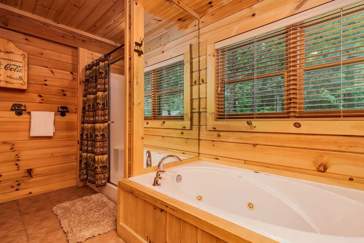 A spa-inspired bathroom with a jacuzzi tub surrounded by wooden paneling, a large mirror, and a window with blinds for privacy. The setup evokes relaxation and luxury, perfect for soaking after a long day.