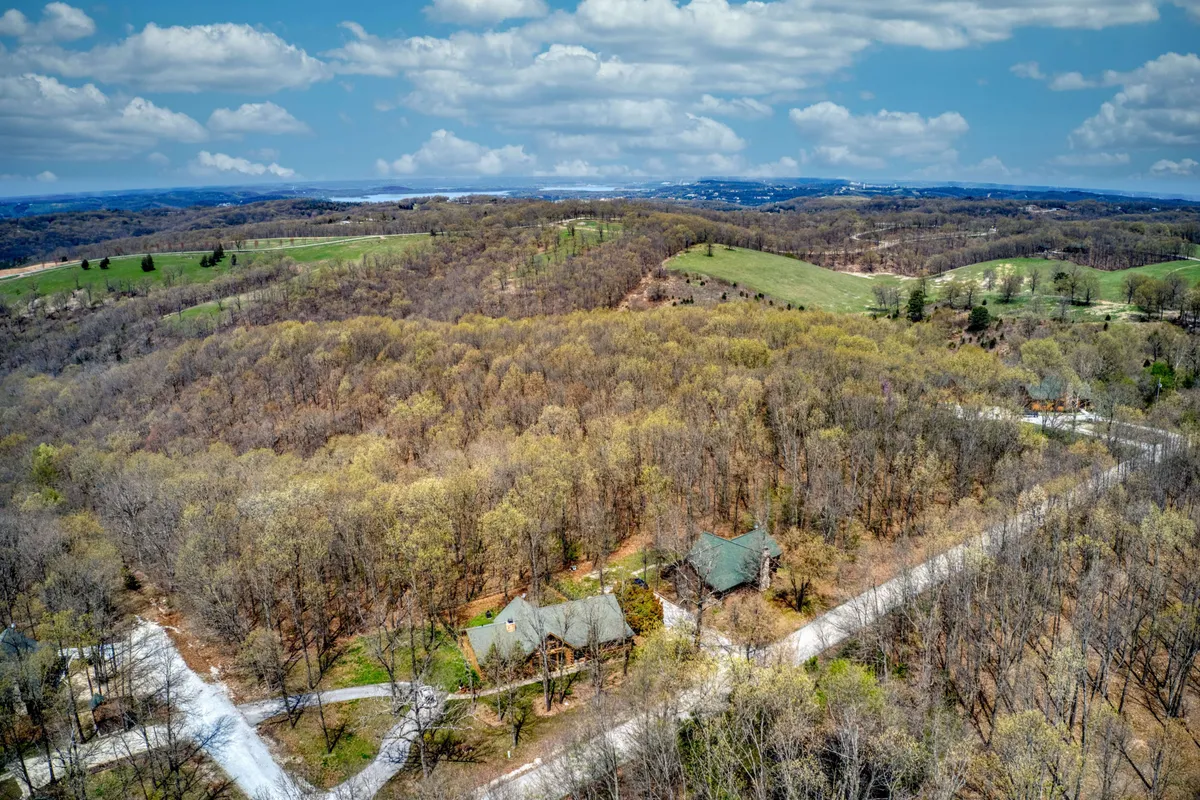 This scene captures two houses set amidst rolling hills, woods, and a meandering road, evoking the expansiveness of the Ozark countryside. The view suggests opportunities for exploration, nature walks, and adventure beyond the immediate cabin grounds.