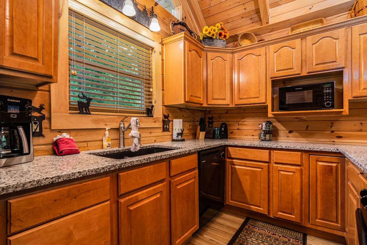 A bright, homey kitchen with granite countertops, wooden cabinets, modern appliances, and a window providing plenty of natural light. The large counter space and accessible layout suggest an ideal spot for group meal prepping, baking, or enjoying morning coffee.