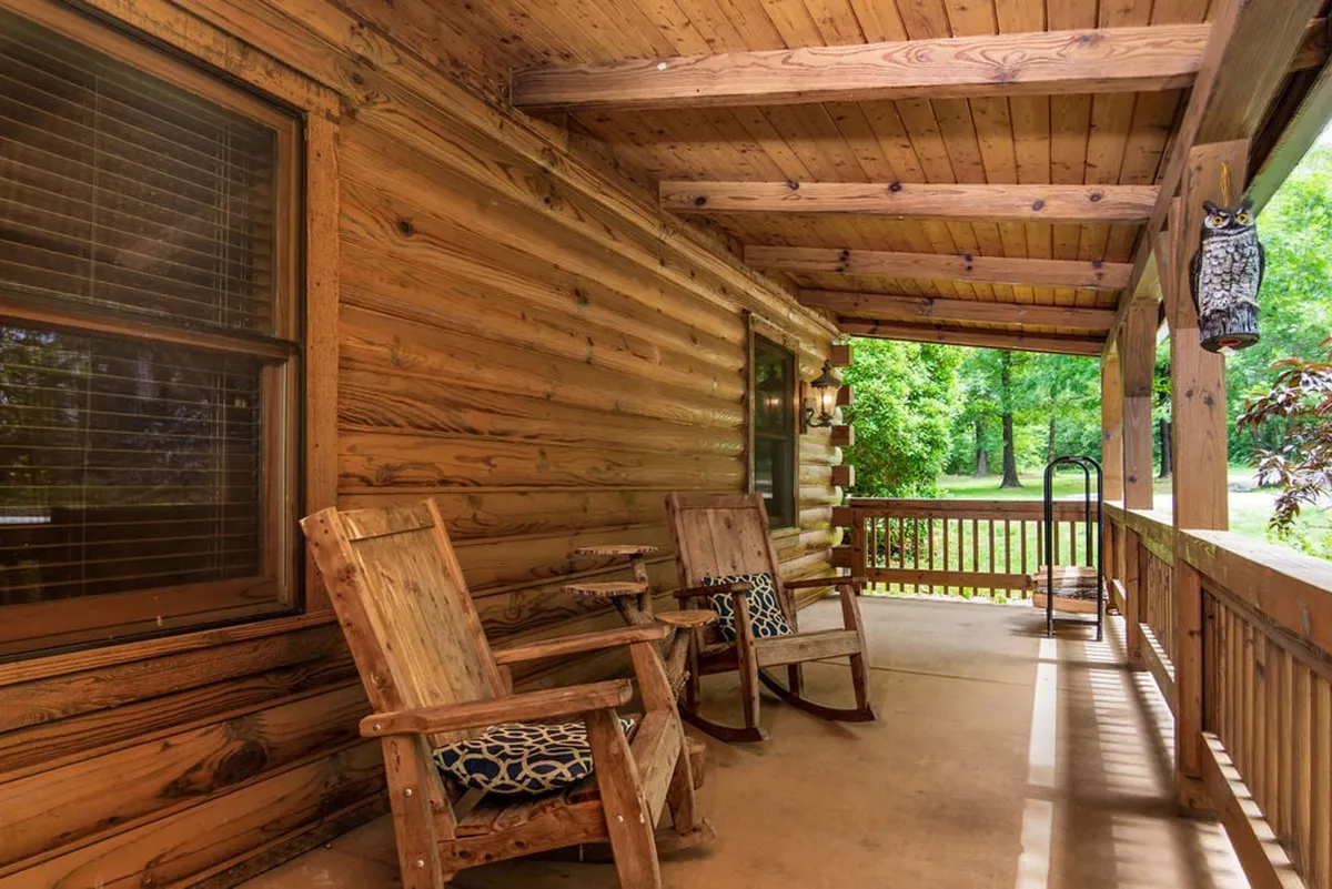 A peaceful outdoor area with wooden rocking chairs on a porch, set against a backdrop of lush greenery. The image conveys a sense of relaxation and a deep connection to the surrounding nature.
